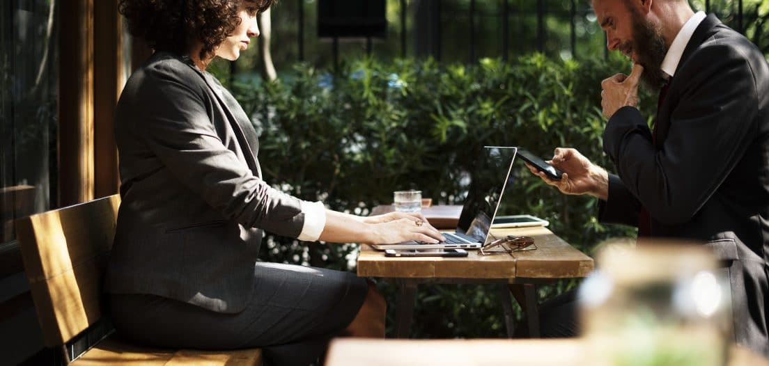 A business man and woman working at a laptop, outside on a sunny day