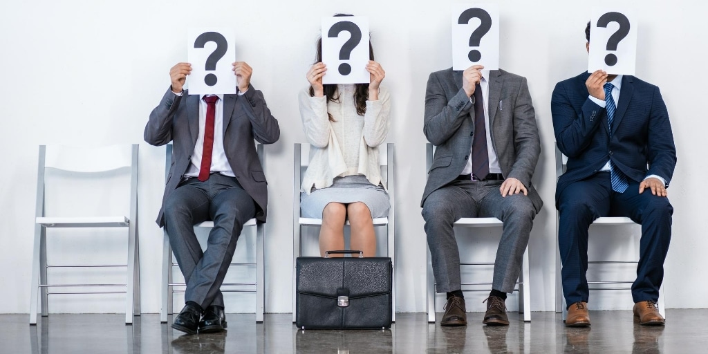 Candidates sitting in a line waiting to be interviewed with question marks in front of their faces