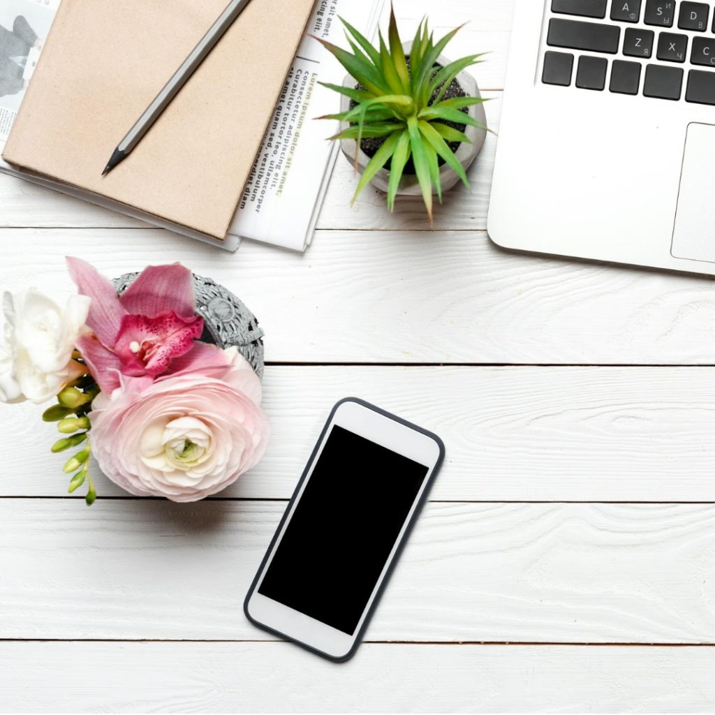 Chic looking workspace, clutter free except for a laptop, phone workbook, a plant and elegant flower arrangement