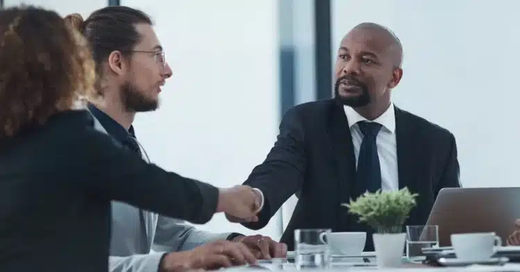 A newly hired black senior executive shakes hands with a female colleague and chats with another colleague before staring their boards of director meeting