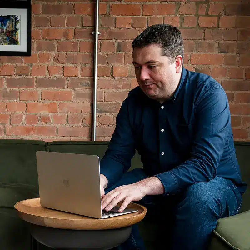 Ryan Davy types on his laptop, sat on the sofas