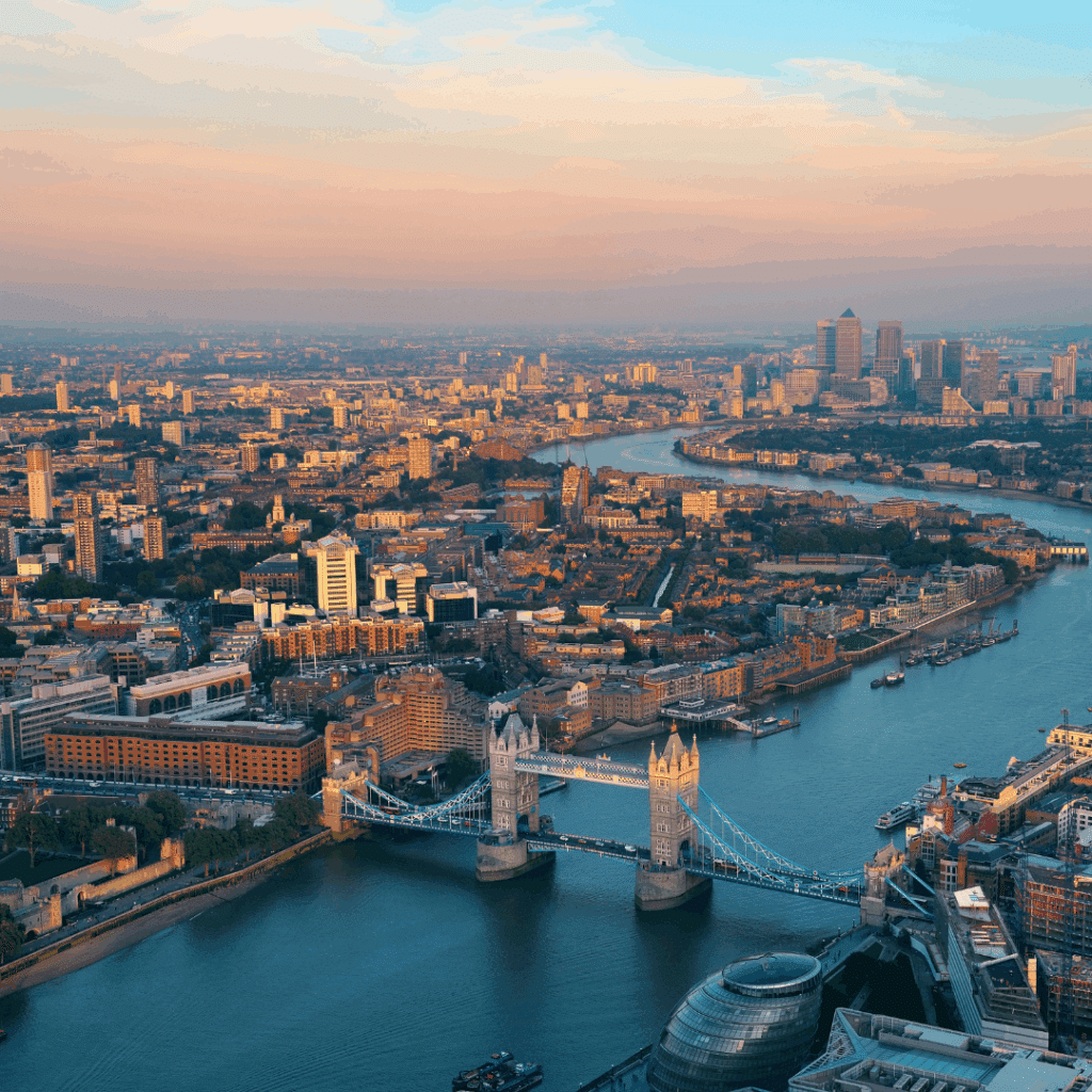 Stunning panoramic view of London at sunset featuring Tower Bridge spanning the River Thames with Canary Wharf in the distance.