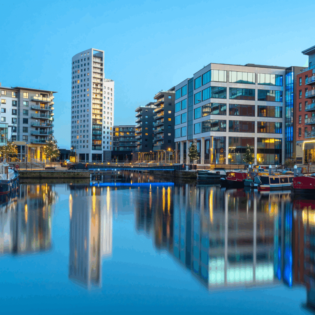 Modern buildings and colourful canal boats reflected in calm waters at Leeds Dock during blue hour.