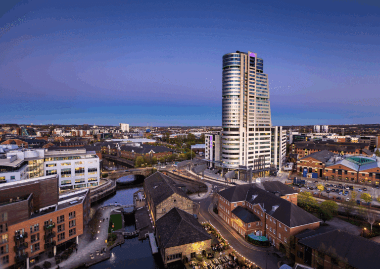 A panoramic view of Leeds city centre at dusk featuring the Bridgewater Place skyscraper, surrounding buildings, and a canal below.