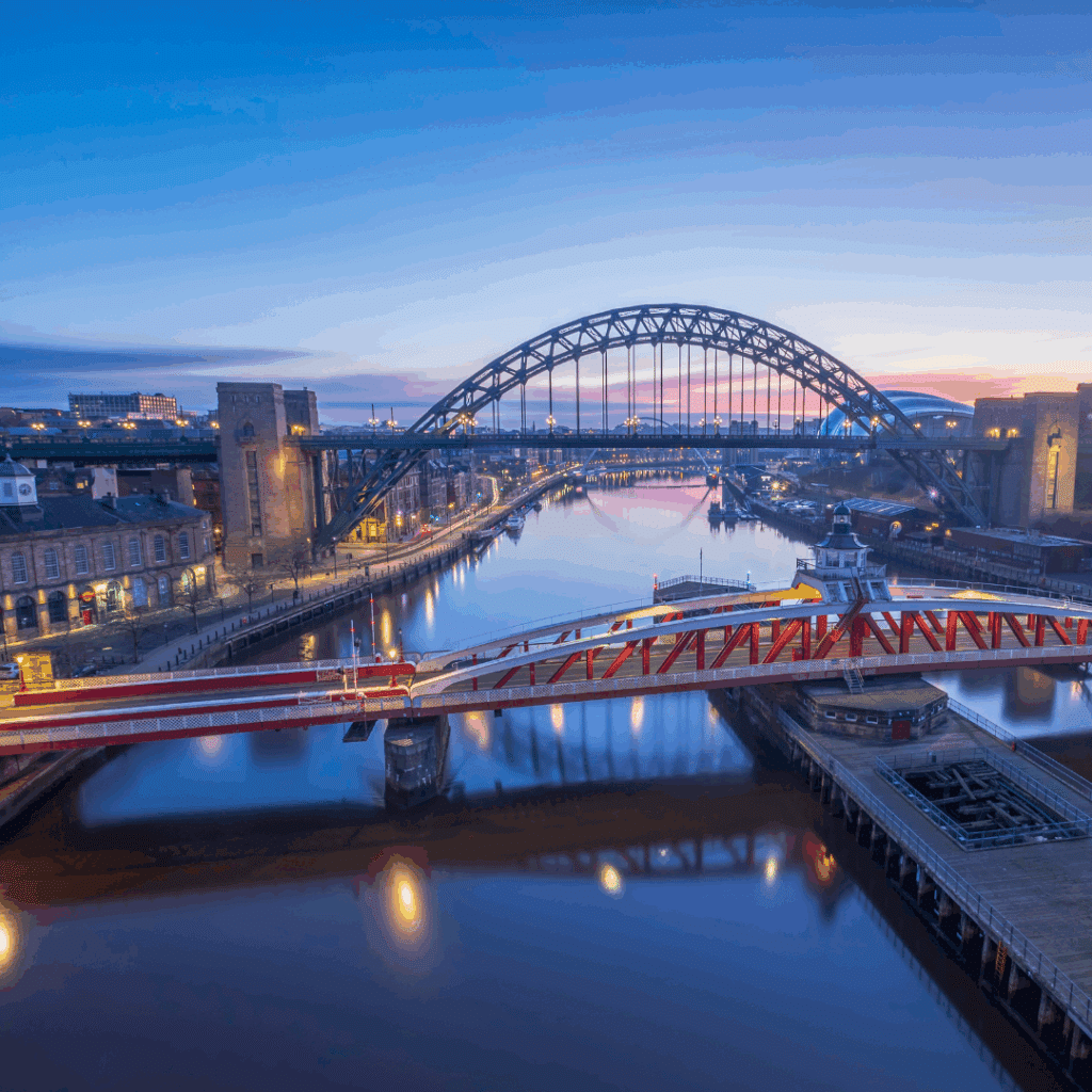 A scenic view of the Tyne Bridge in Newcastle, reflecting in the River Tyne under a vibrant evening sky.