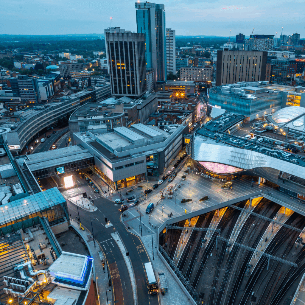 Aerial view of Birmingham city centre showing modern buildings, roads, and New Street Station at dusk.