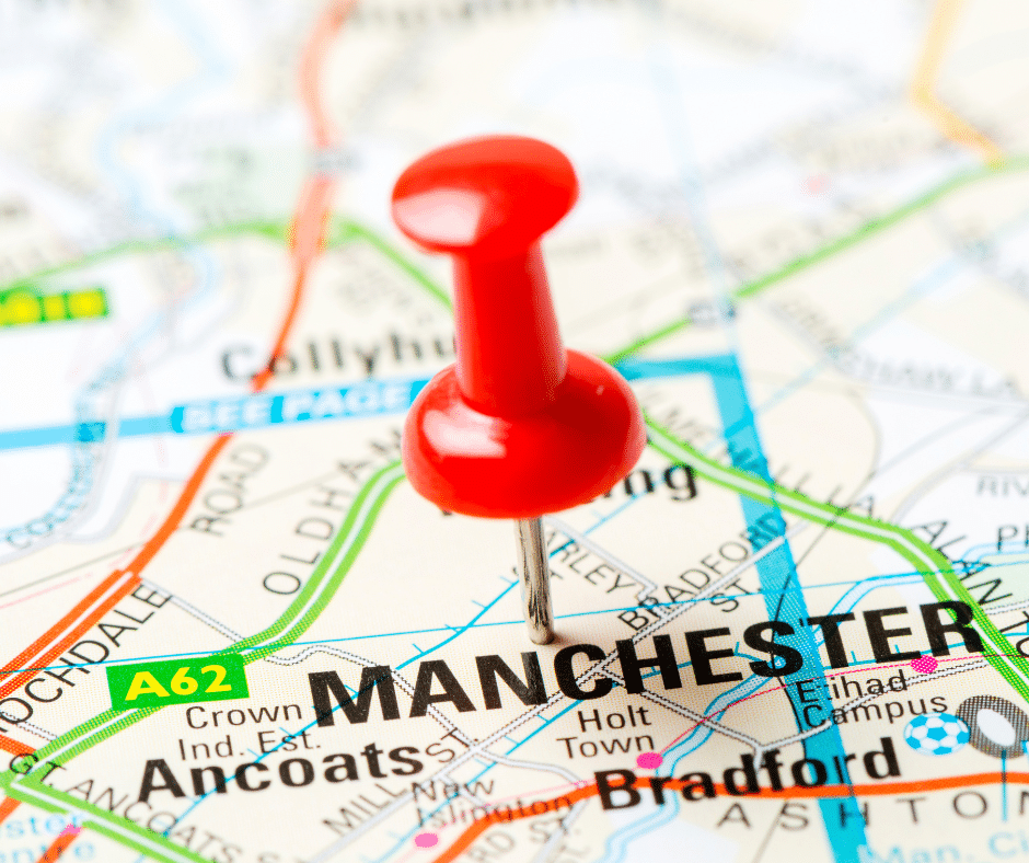 Close-up of a printed map showing Manchester, UK, marked with a red pushpin near Ancoats and the A62 road.