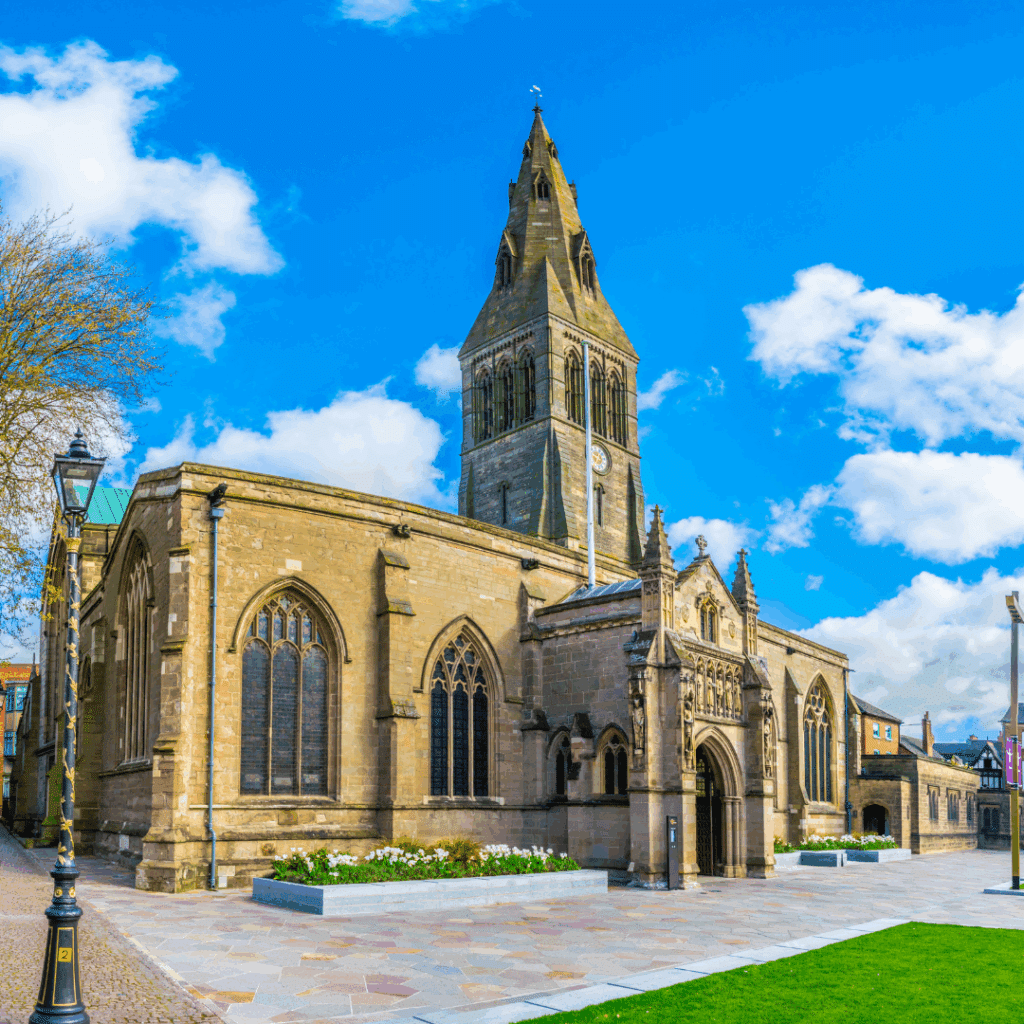 The historic Leicester Cathedral with its tall spire and gothic architecture under a blue sky.