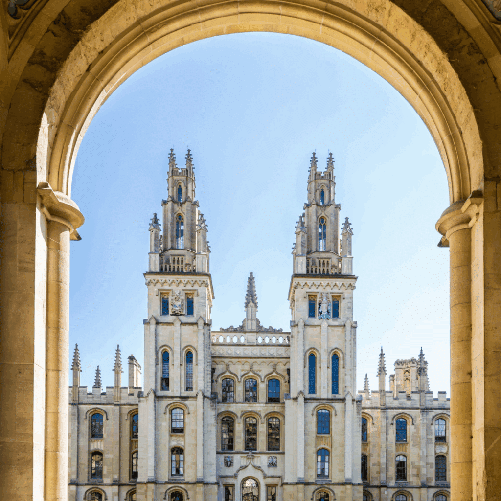 View through a stone archway framing the grand twin spires of the University of Oxford’s All Souls College building on a clear day.