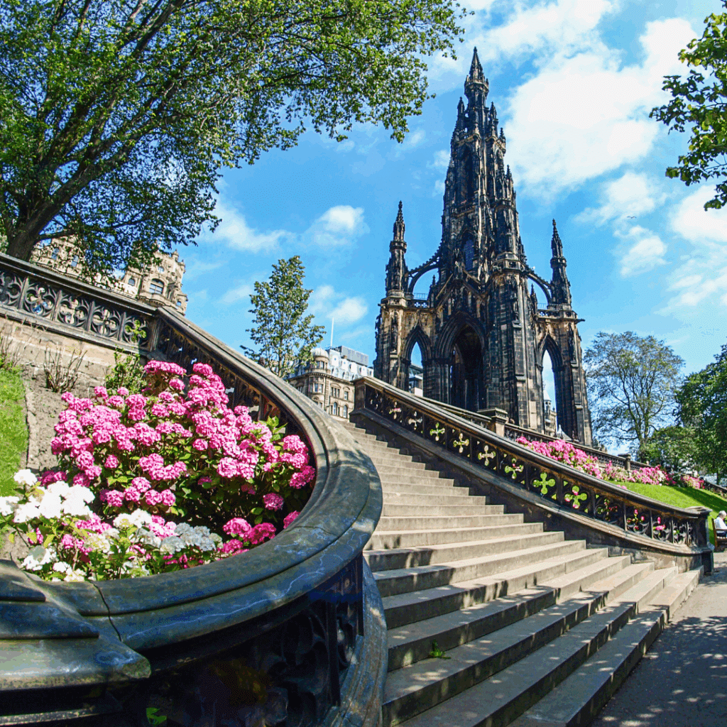 The Scott Monument rising above Princes Street Gardens, framed by pink flowers and an ornate staircase.
