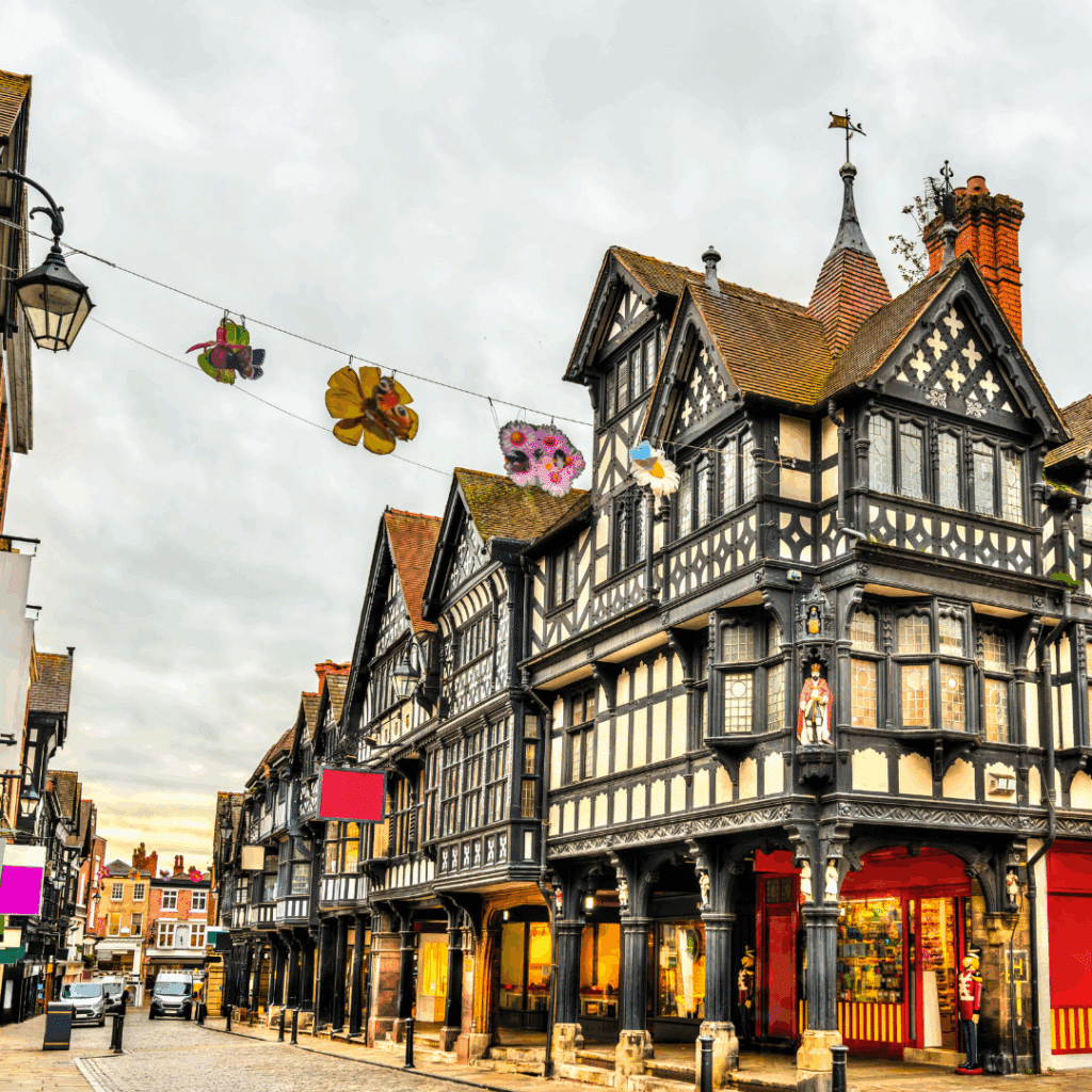 Traditional black-and-white Tudor architecture lining a cobbled street in Chester, decorated with hanging floral banners.