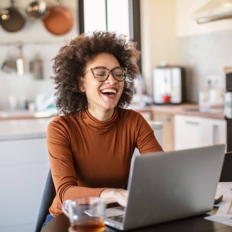 Woman smiling while working on a laptop in her kitchen