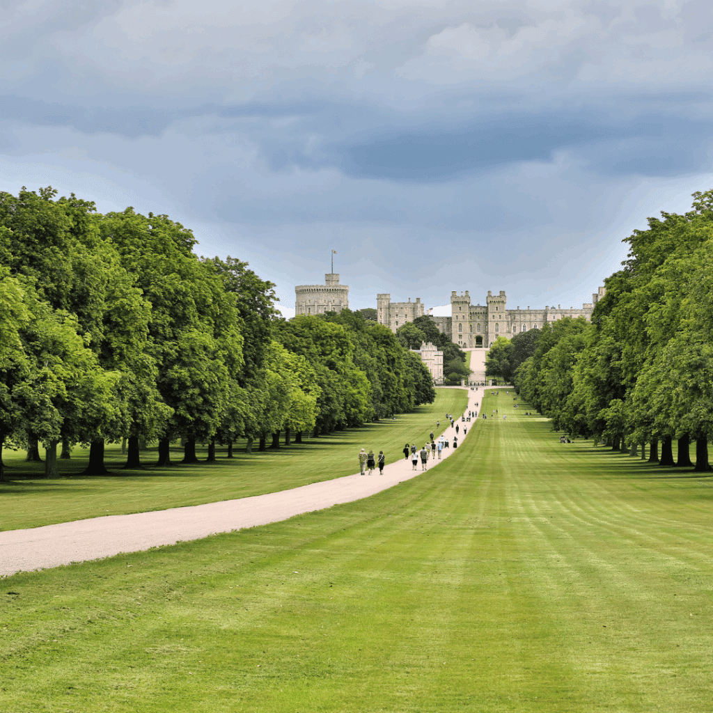 A wide grassy path known as the Long Walk leading up to Windsor Castle, lined with trees and visitors walking.