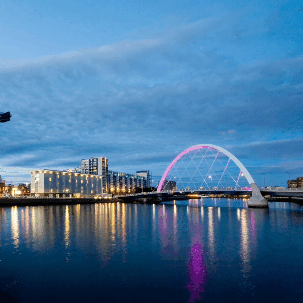 Clyde Arc bridge in Glasgow illuminated with purple lights reflecting on the River Clyde at dusk.