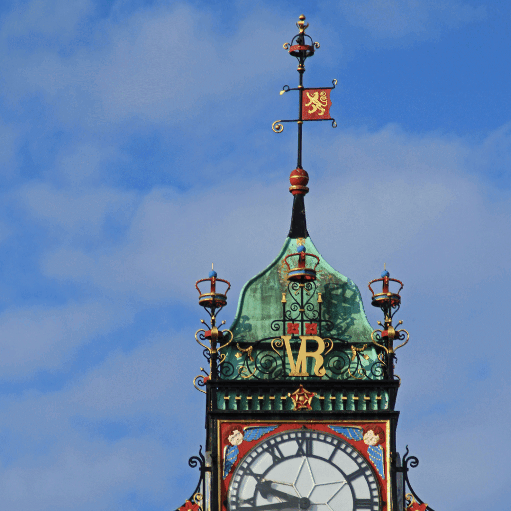 Close-up of the Eastgate Clock’s intricate Victorian design, with a red and gold weather vane against a blue sky.