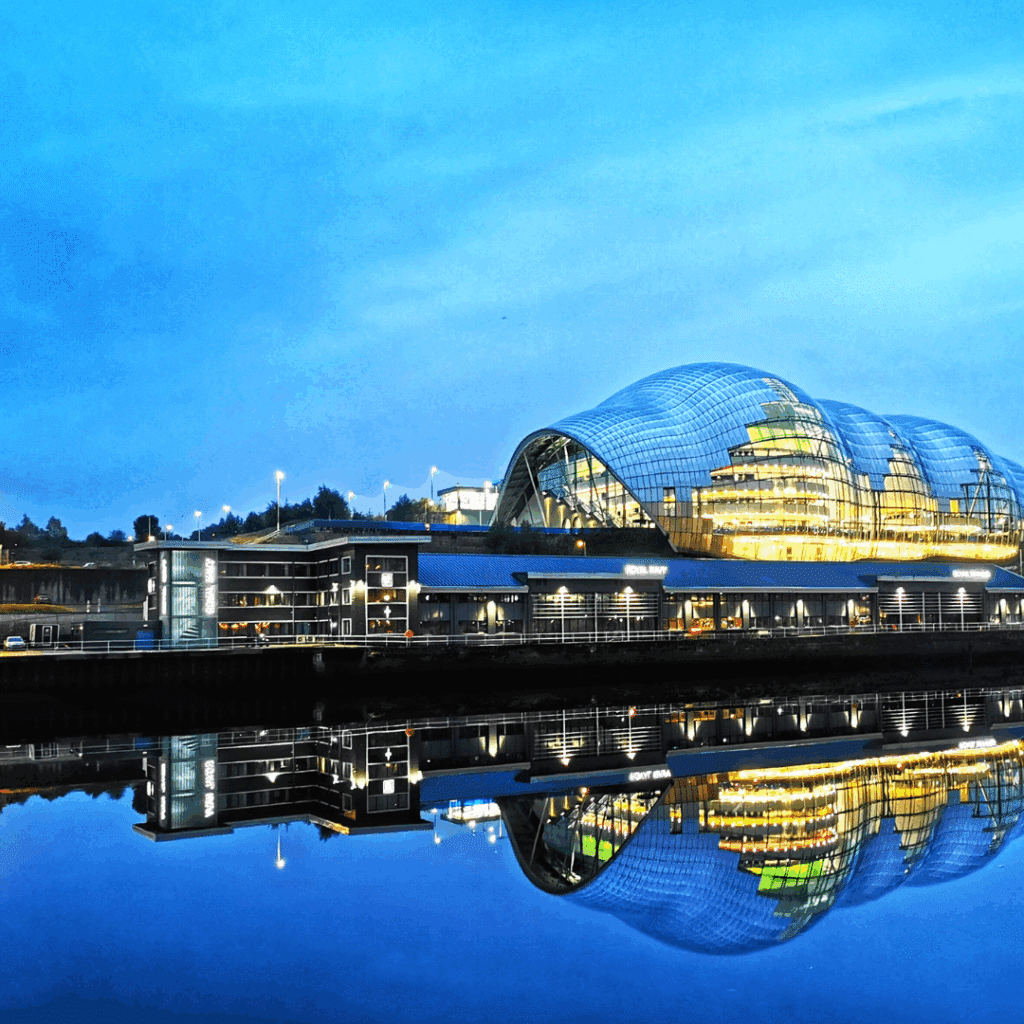 The Sage Gateshead concert venue in Newcastle, glowing with vibrant lights and reflecting perfectly in the River Tyne.