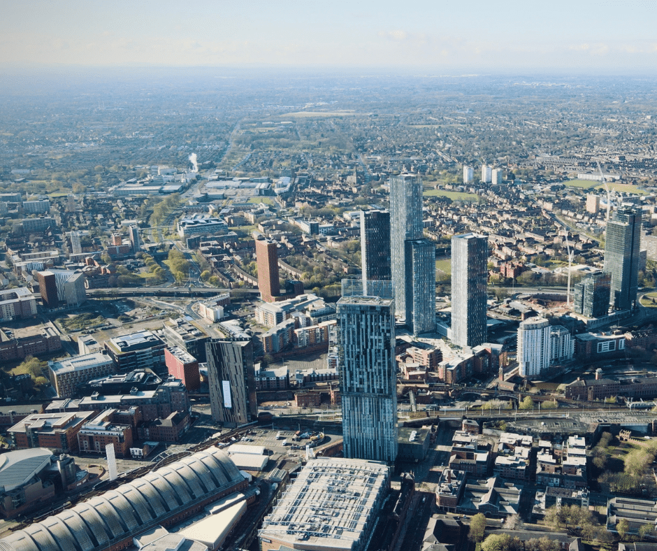 Elevated view of Manchester featuring tall residential skyscrapers, sprawling suburbs, and the city's urban layout.