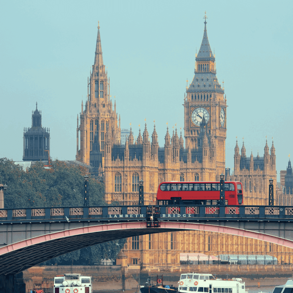 A red London bus crossing Lambeth Bridge with the Houses of Parliament and Big Ben in the background.