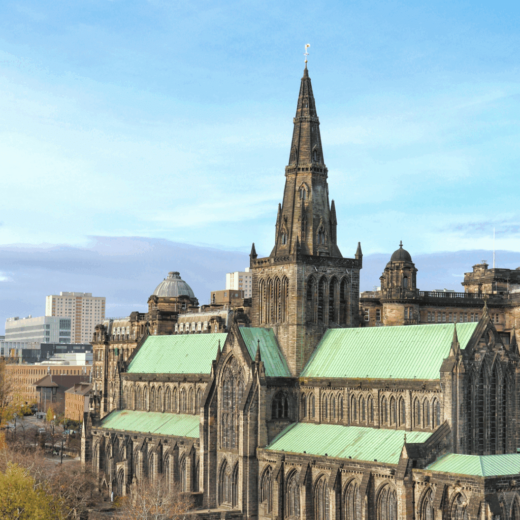 Glasgow Cathedral with its prominent spire and green roof against a blue sky.