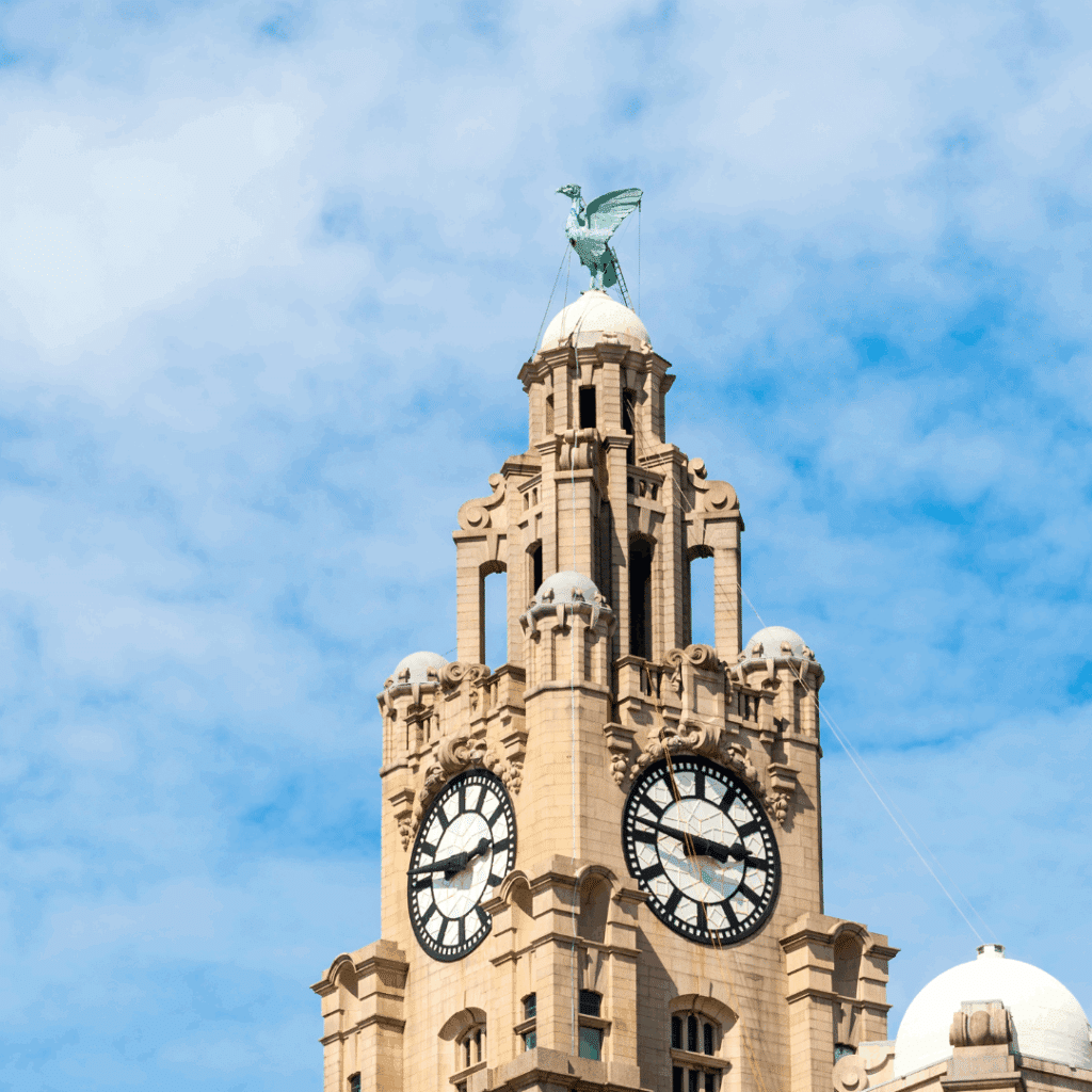 Close-up of the Liver Building clock tower in Liverpool with the iconic Liver Bird perched on top under a blue sky.
