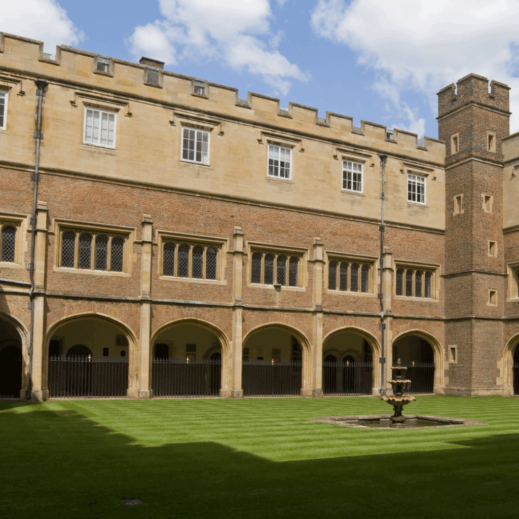 Historic red brick courtyard of Eton College with arched walkways and a small fountain on the grass.