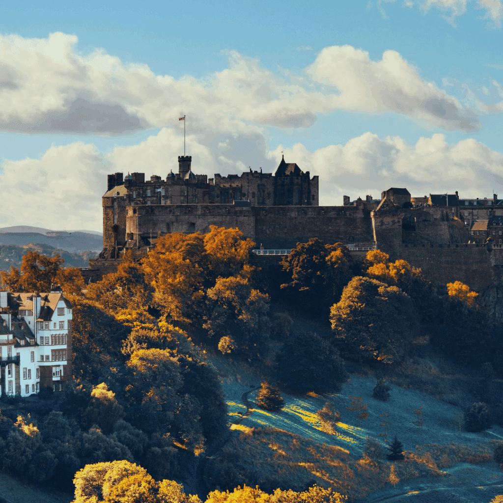 Edinburgh Castle viewed from a distance surrounded by autumn-colored trees and historic buildings.