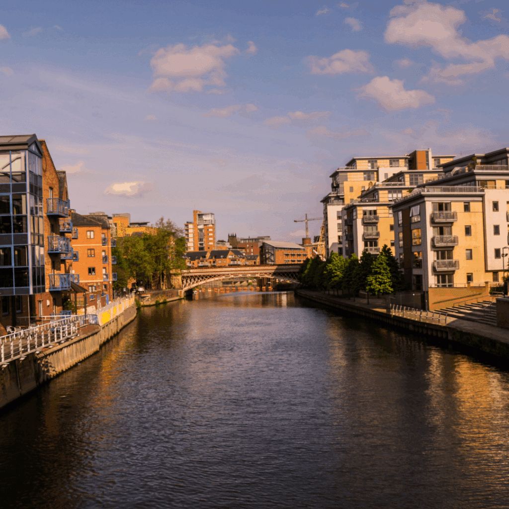 Sunny riverside view in Leeds with residential flats and footbridge along the River Aire.