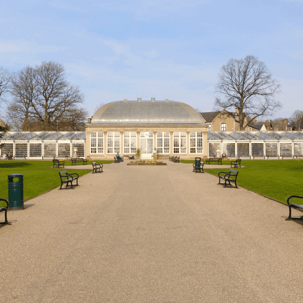 The grand glass pavilion of Sheffield Botanical Gardens surrounded by green lawns and park benches.