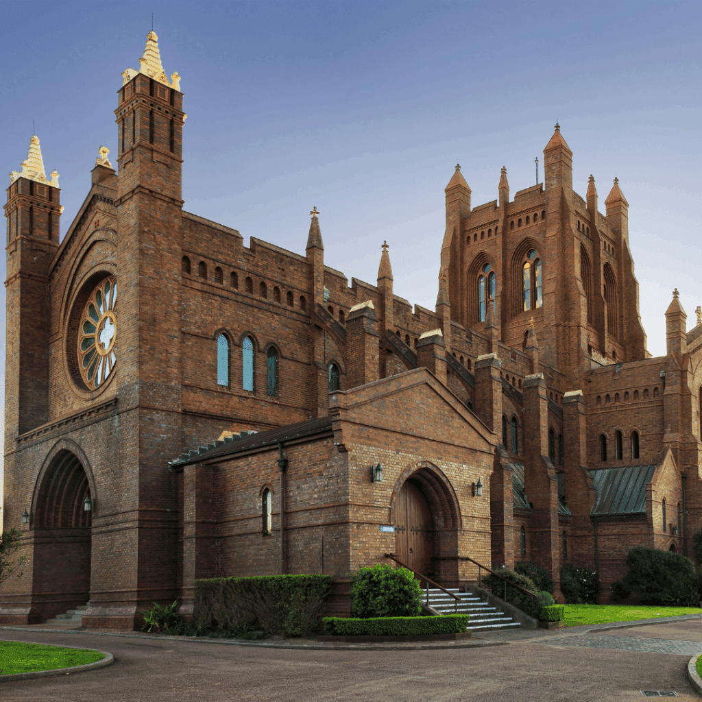 A striking red-brick Gothic church in Newcastle, featuring tall towers and intricate architecture under a twilight sky.