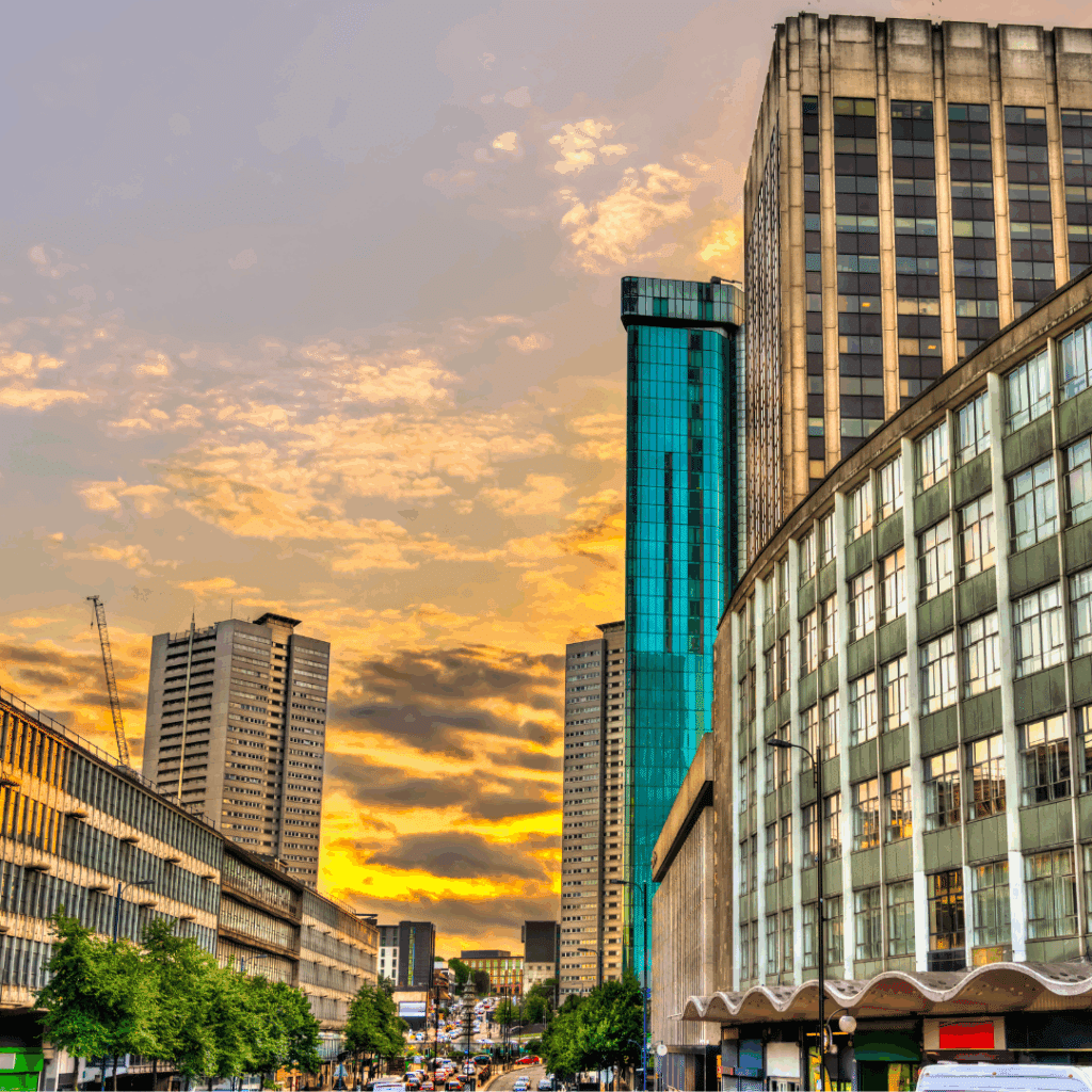 Birmingham city skyline at sunset featuring tall modern buildings and a vibrant orange sky.