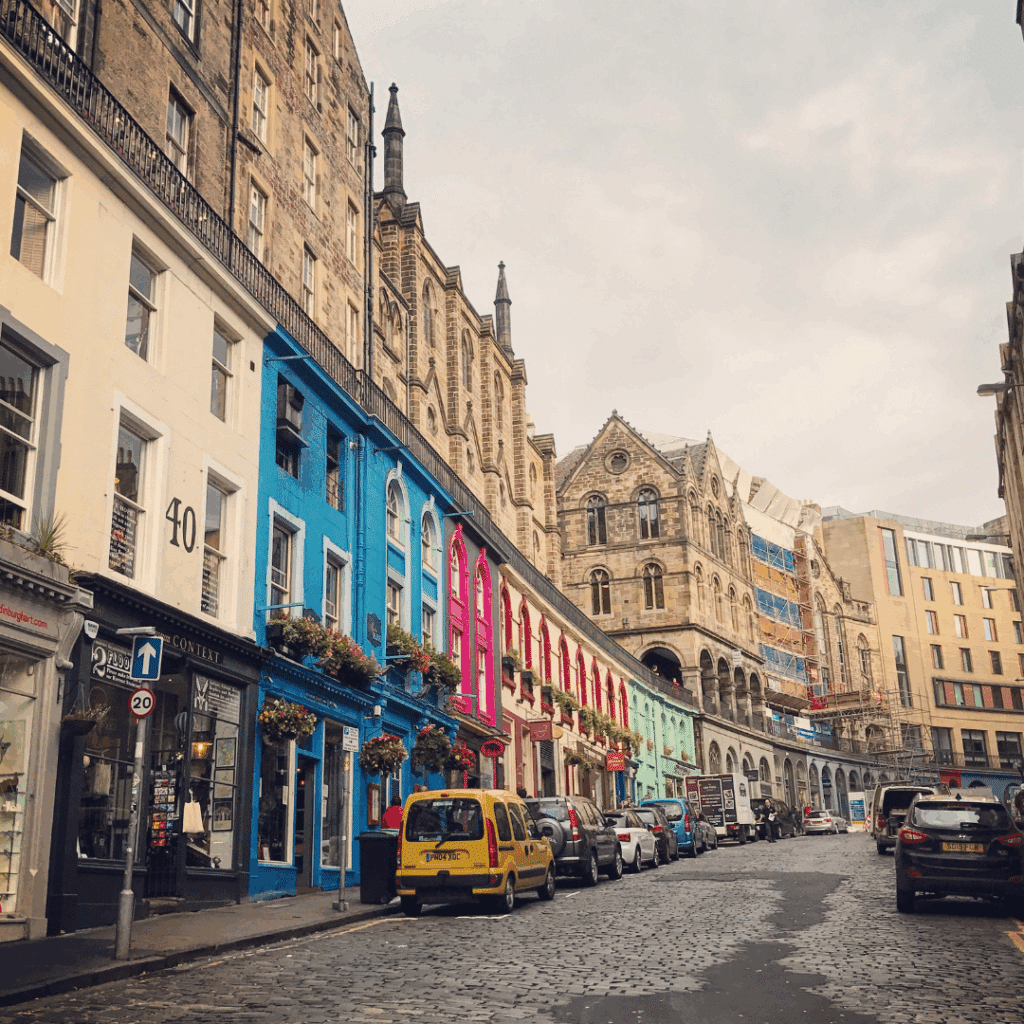 Colourful buildings lining Victoria Street in Edinburgh, with parked cars and a cobbled road.