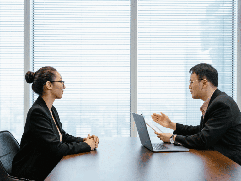 A man and a woman in a formal interview across a desk in an office.