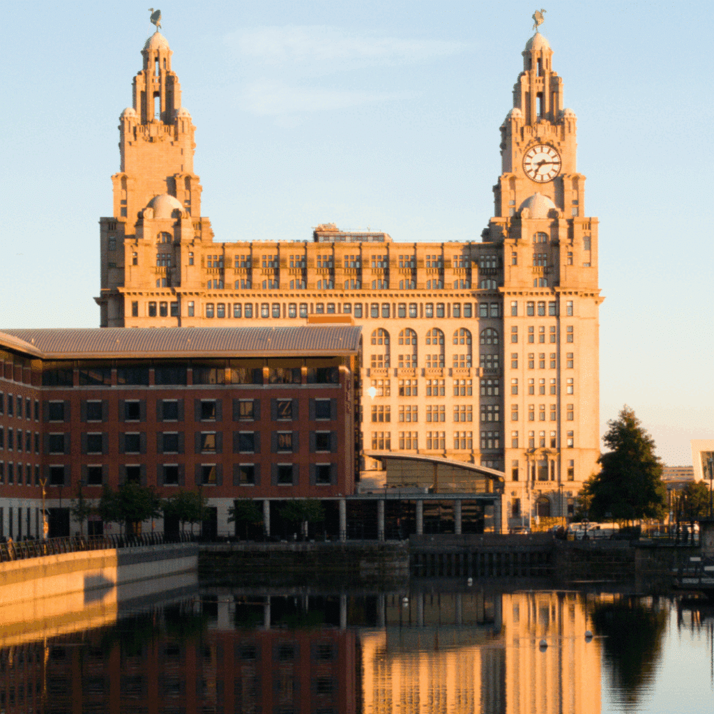 Liverpool’s Royal Liver Building bathed in warm sunset light with its twin clock towers and nearby modern buildings.