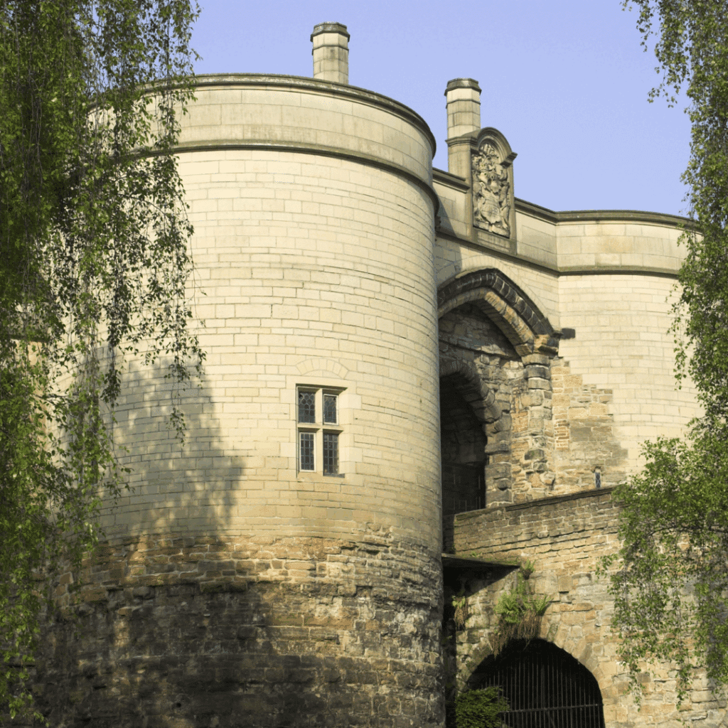 The stone entrance of Nottingham Castle with round towers, historic architecture and leafy trees partially framing the view.