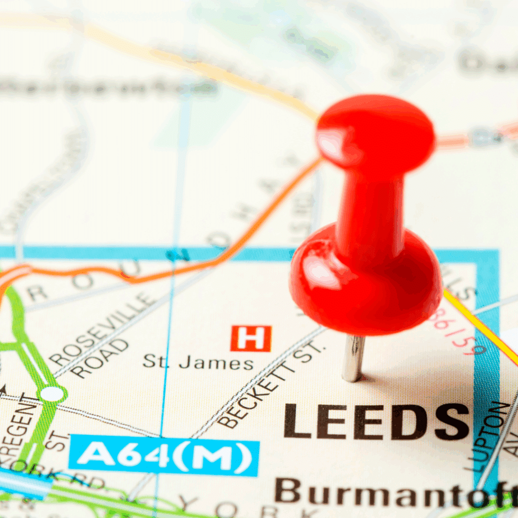 Macro shot of a map with a red pushpin marking the city of Leeds, with nearby roads and landmarks visible.