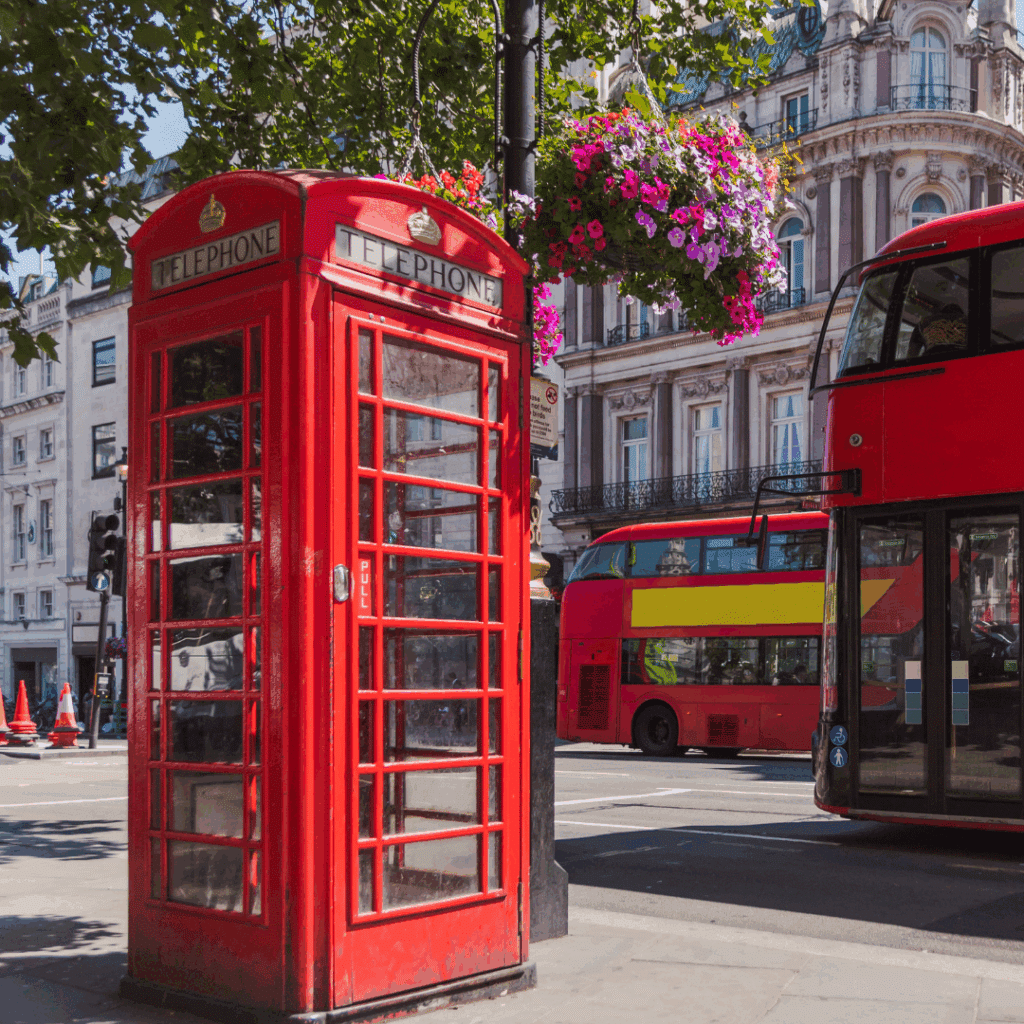A vibrant red phone booth and London bus on a sunny street in central London, with hanging flower baskets