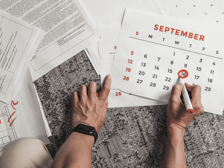 Person marking the 16th on a printed September calendar, surrounded by documents.