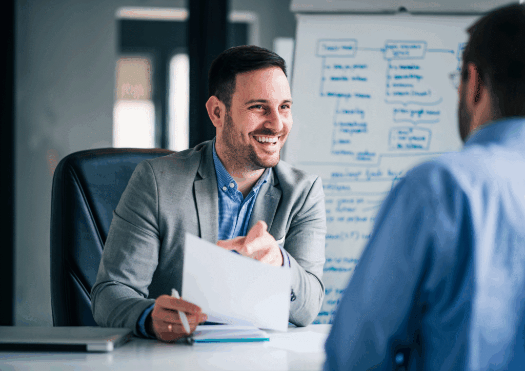 A smiling interviewer holding a resume during a discussion with a job candidate in an office setting. He is a c# software developer
