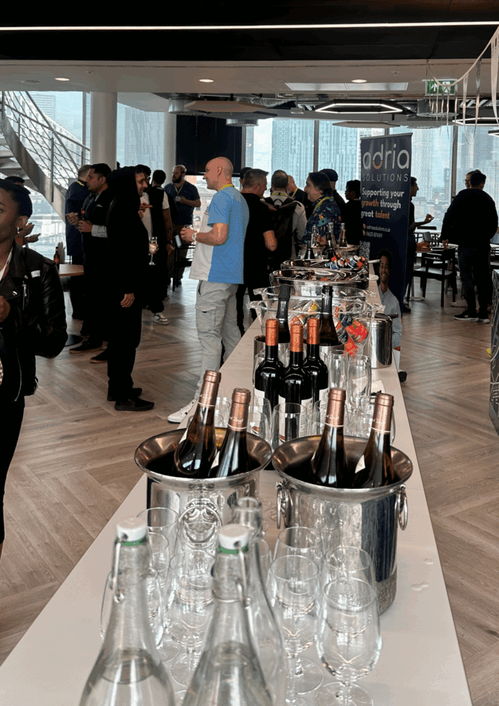 Attendees mingling and chatting beside a long table filled with bottles of wine, beer, and glasses at an indoor networking event.
