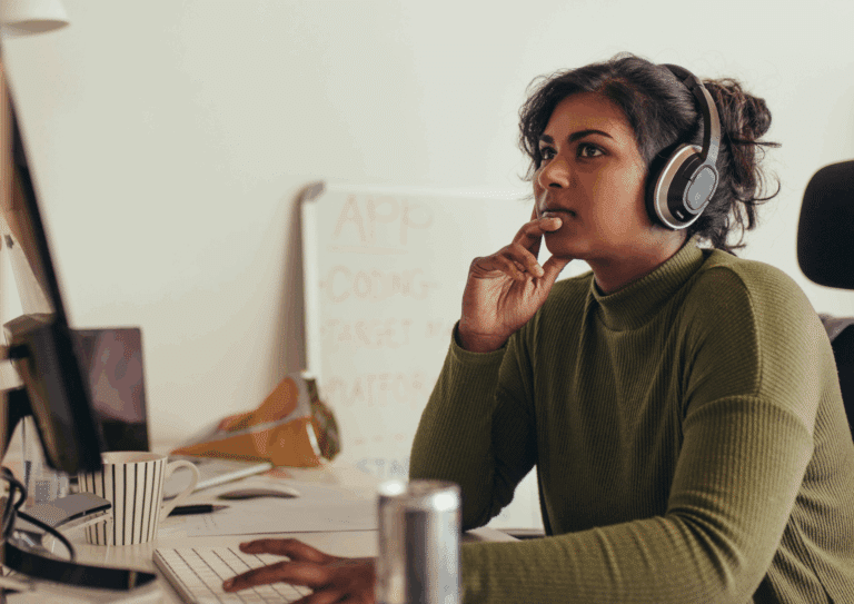 Woman wearing headphones focused on a computer screen in a modern office environment