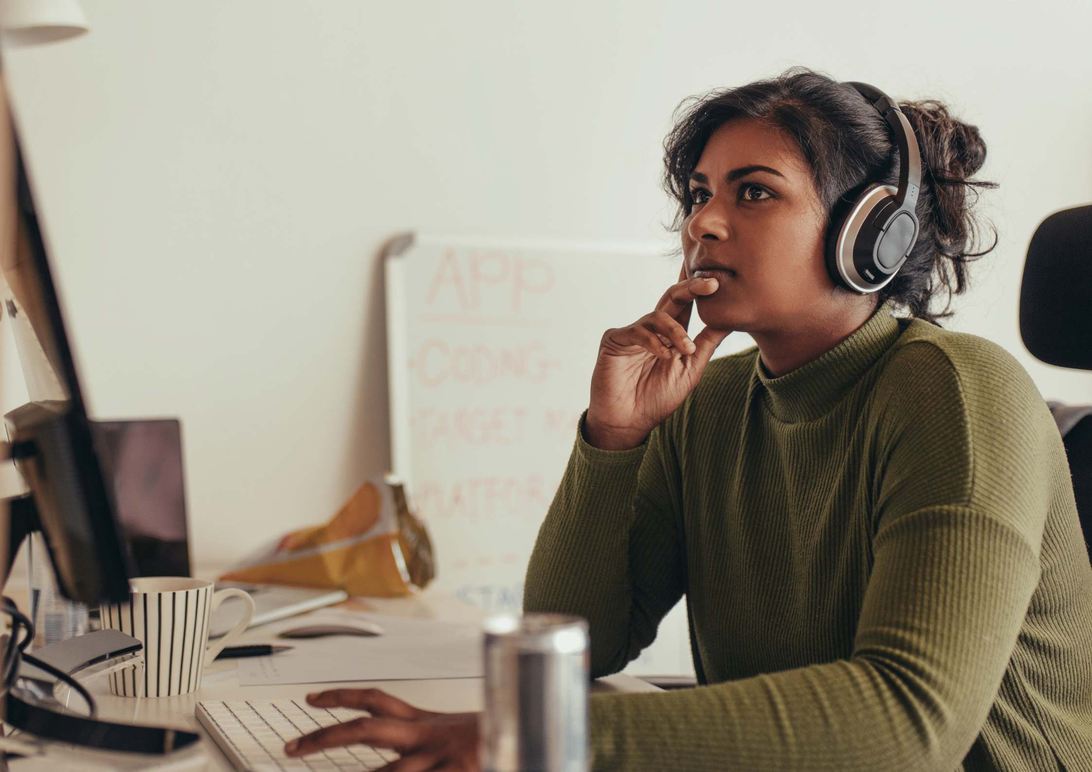 Woman wearing headphones focused on a computer screen in a modern office environment