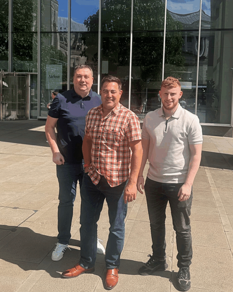 Three men standing confidently outside a modern office building, posing in the sunlight after what appears to be a productive meetup.