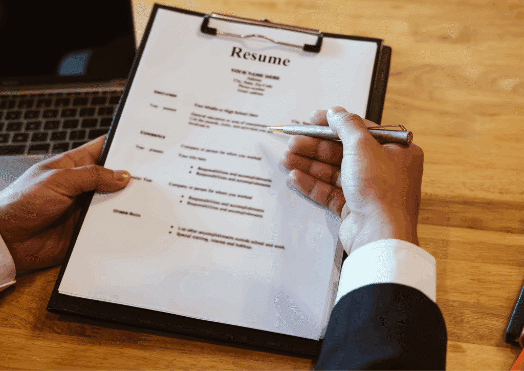 A person holding and pointing to a printed resume on a clipboard during a job application or interview process.