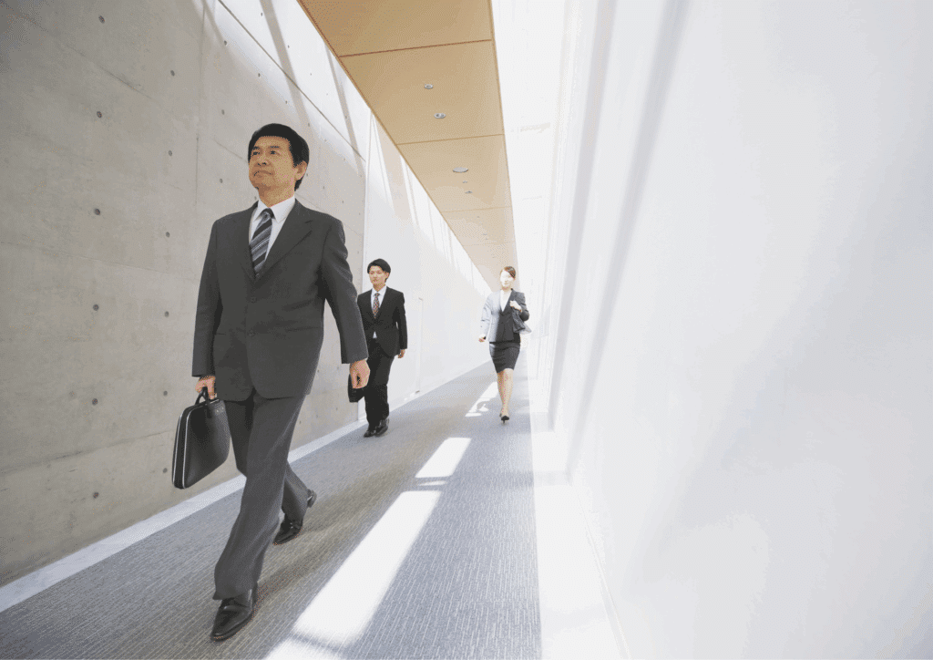 Businessman in a suit carrying a briefcase, walking with colleagues in a bright modern office hallway, symbolizing career progress and new beginnings