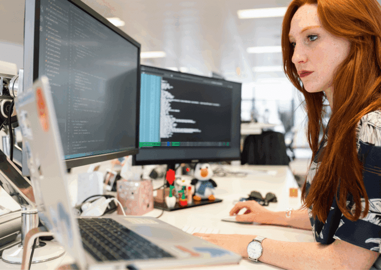 A focused software developer working at a desk with code displayed on two large monitors and a laptop