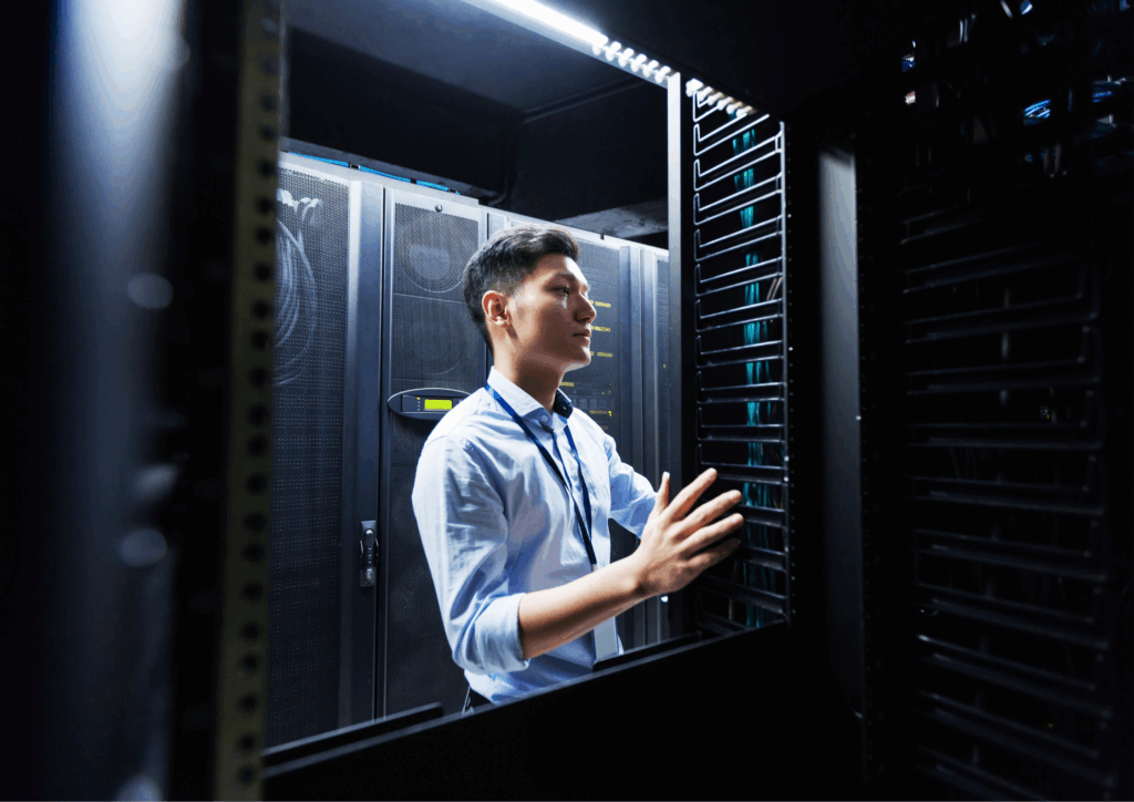 Male IT technician working inside a data center, checking and managing server racks and network equipment.