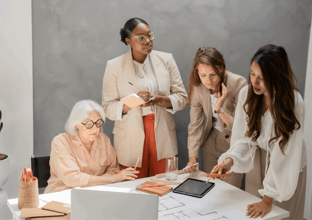 Group of diverse professionals working together around a desk with notebooks, pencils, and digital tablets during a brainstorming session.