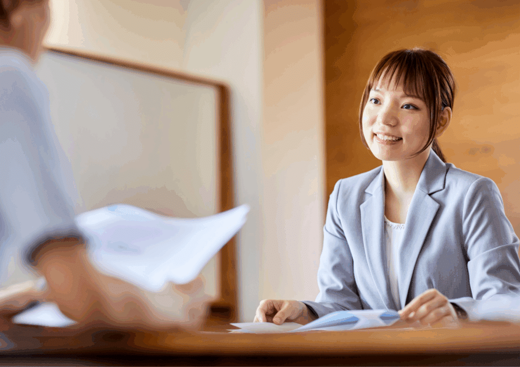 A smiling professional woman in a blazer attending a job interview across the table from a recruiter holding documents