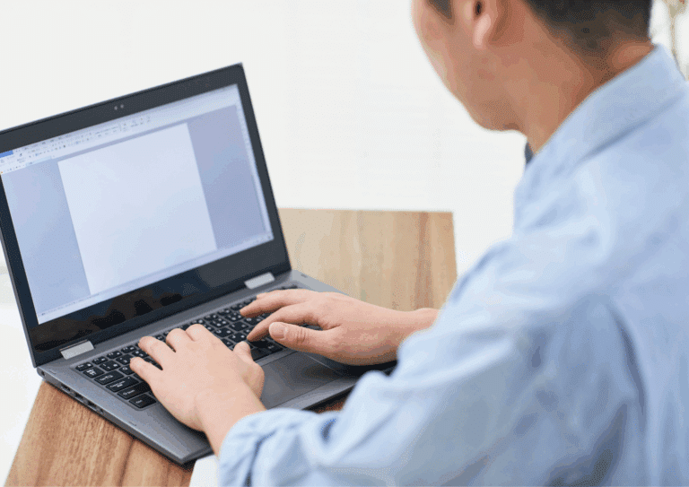 Person typing on a laptop at a desk, representing writing a LinkedIn job announcement post