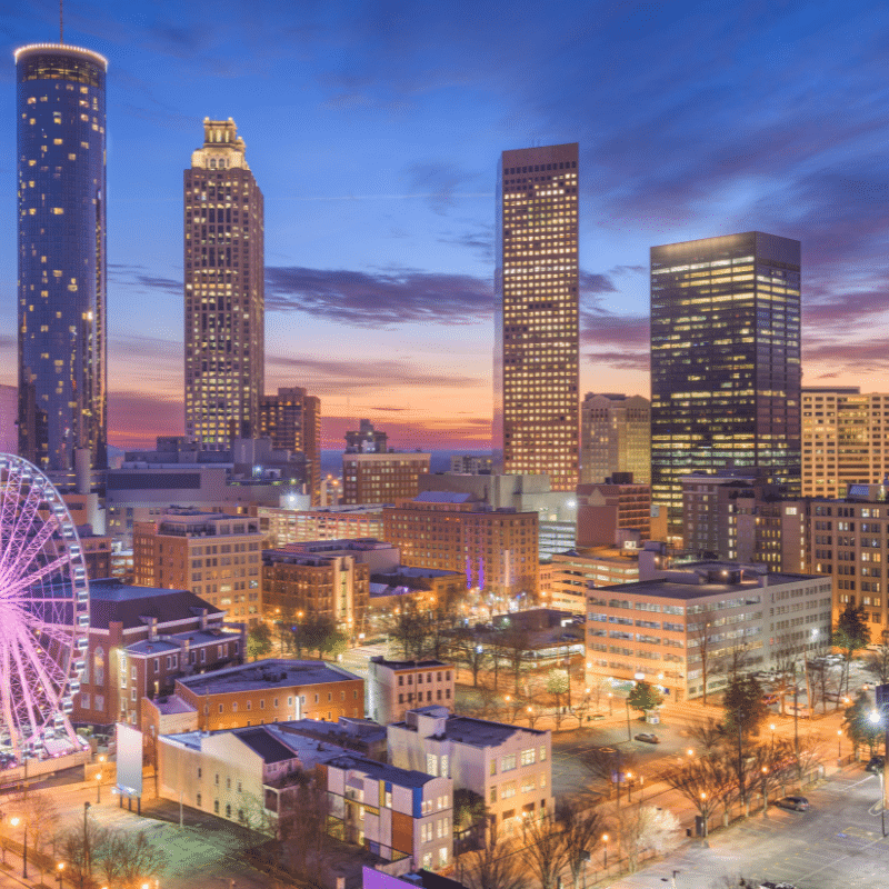 A view of the Atlanta skyline at sunset, featuring illuminated skyscrapers, the SkyView Ferris wheel, and city lights reflecting the vibrant atmosphere of downtown Atlanta.